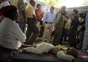 Bill Clinton speaks to the press as a little boy, badly injured in the earthquake, rests